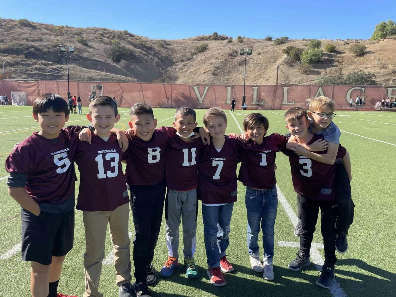 Group of children in maroon jerseys with numbers standing on a green field