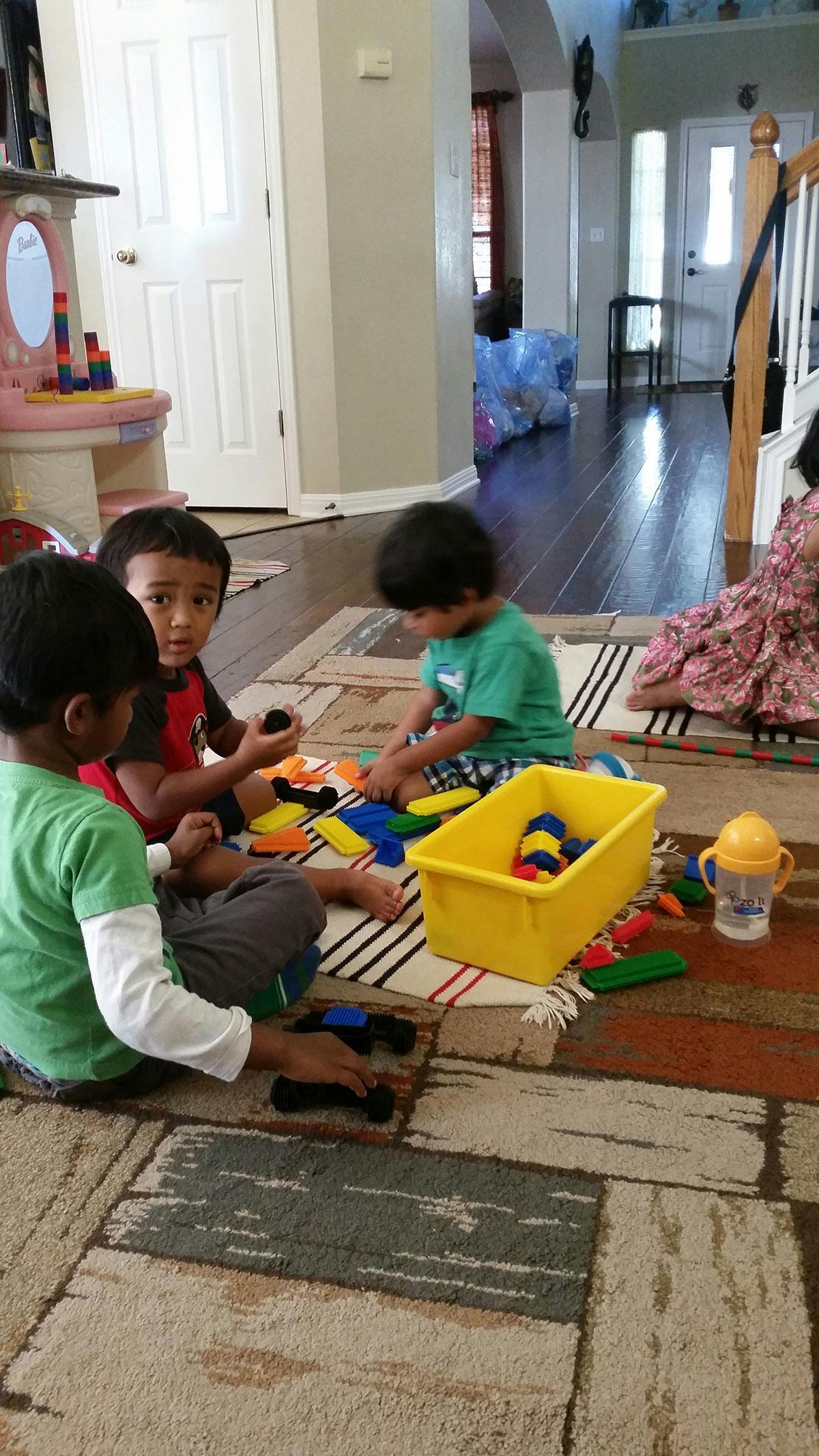 Three children playing with colorful blocks on a rug