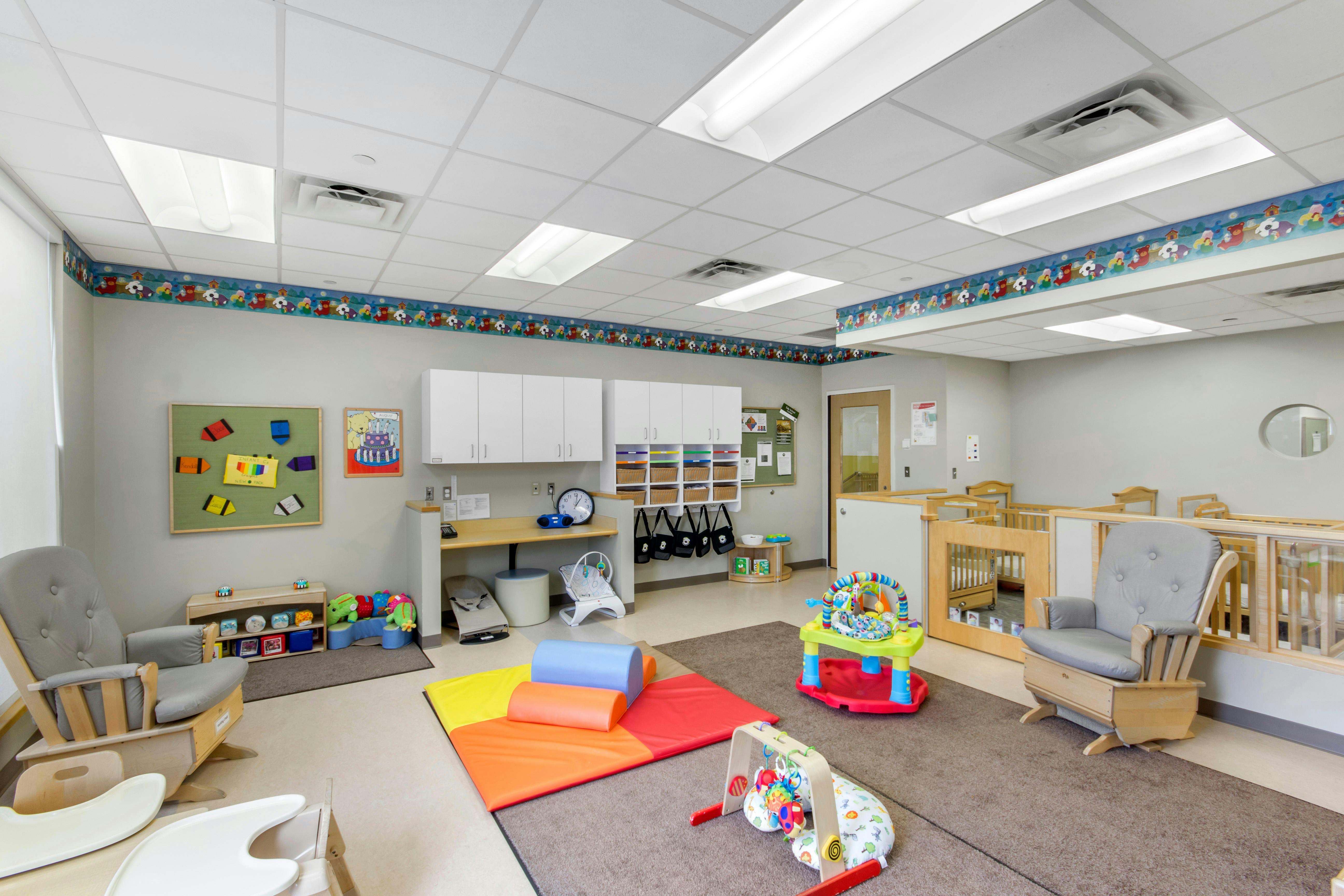 Childcare room with play mats, toys, and cribs