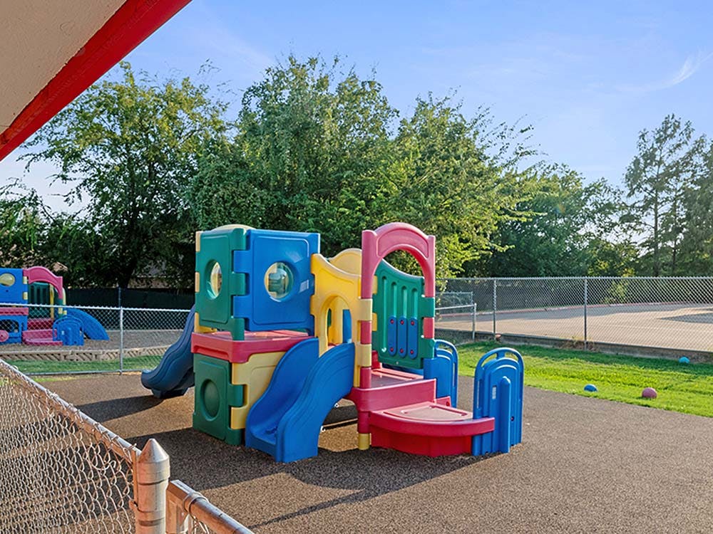 Colorful playground equipment on a soft ground surface with a fence in the foreground