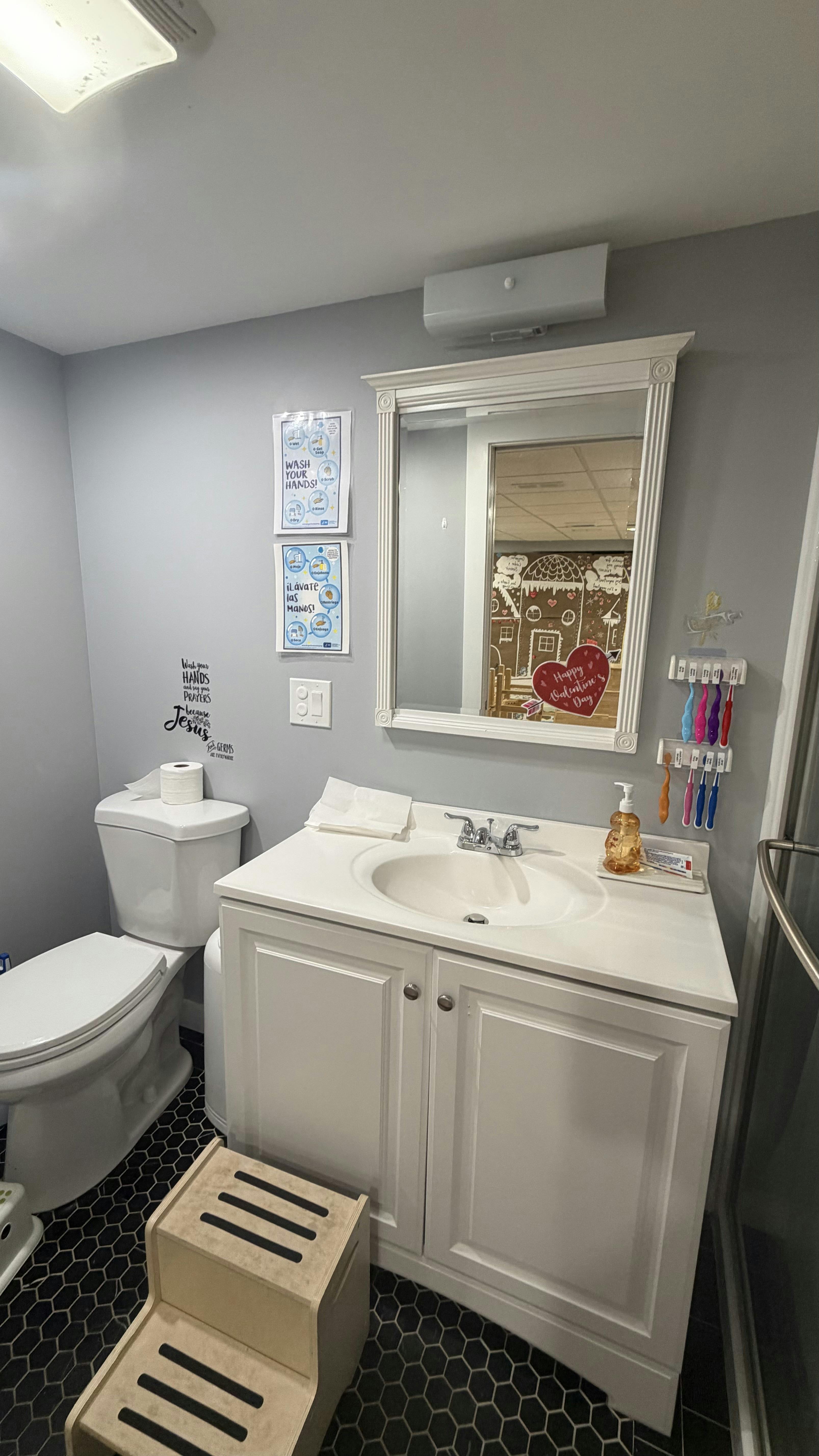 bathroom with a white vanity, sink, mirror, and toilet, with a wooden step stool