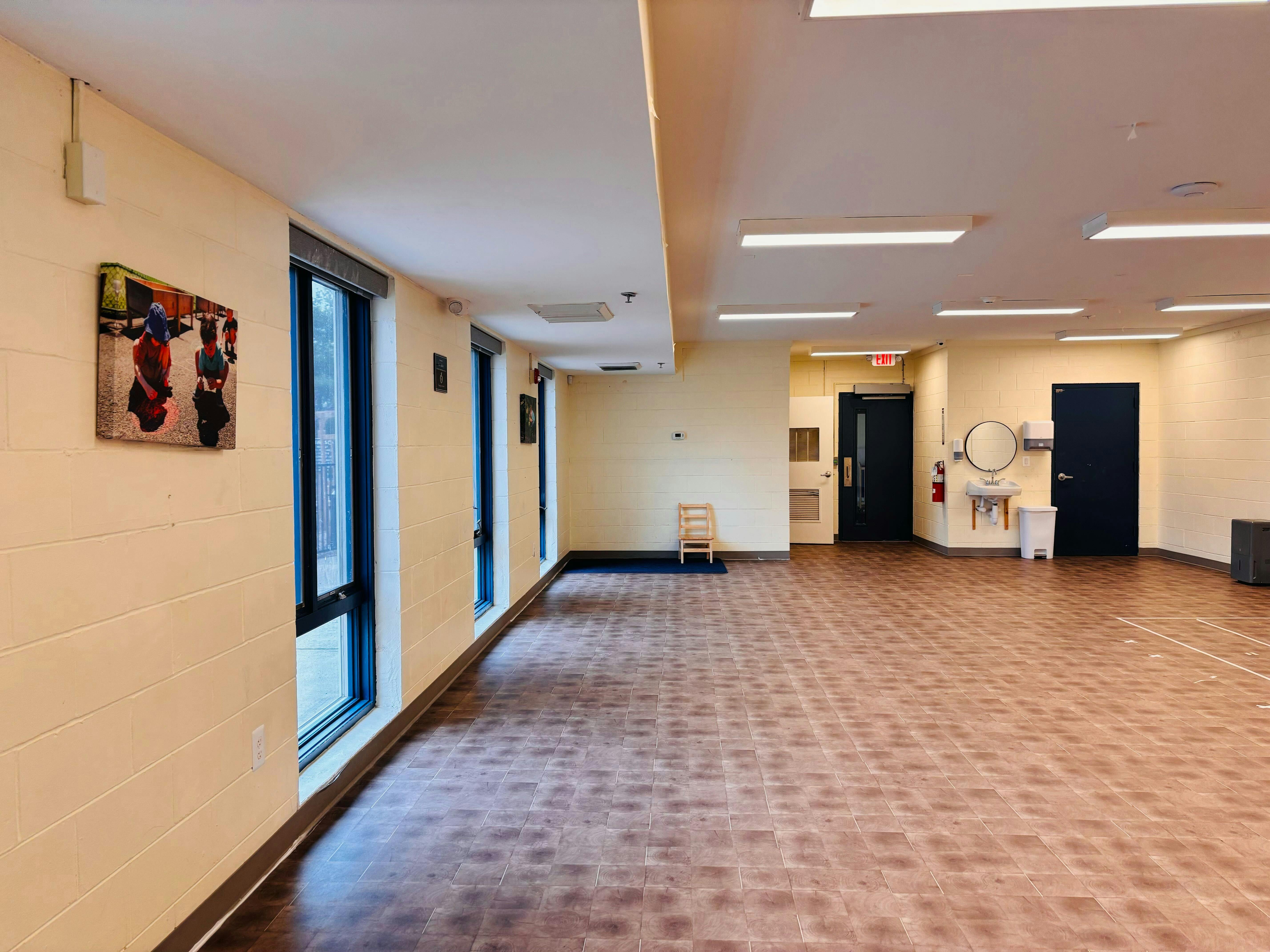 An empty room with tiled floors and light-colored walls, featuring large windows and doors