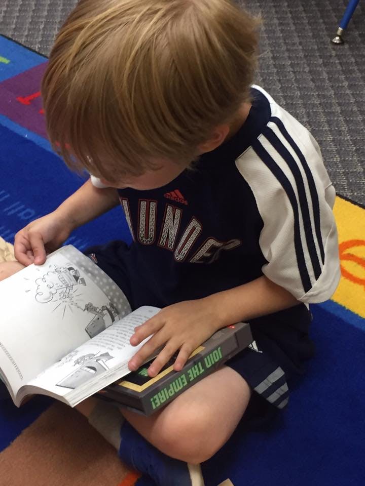 Child reading a book with "JOIN THE EMPIRE!" visible on another book