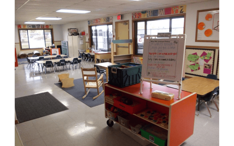 Empty classroom with small tables and chairs, a whiteboard with writing