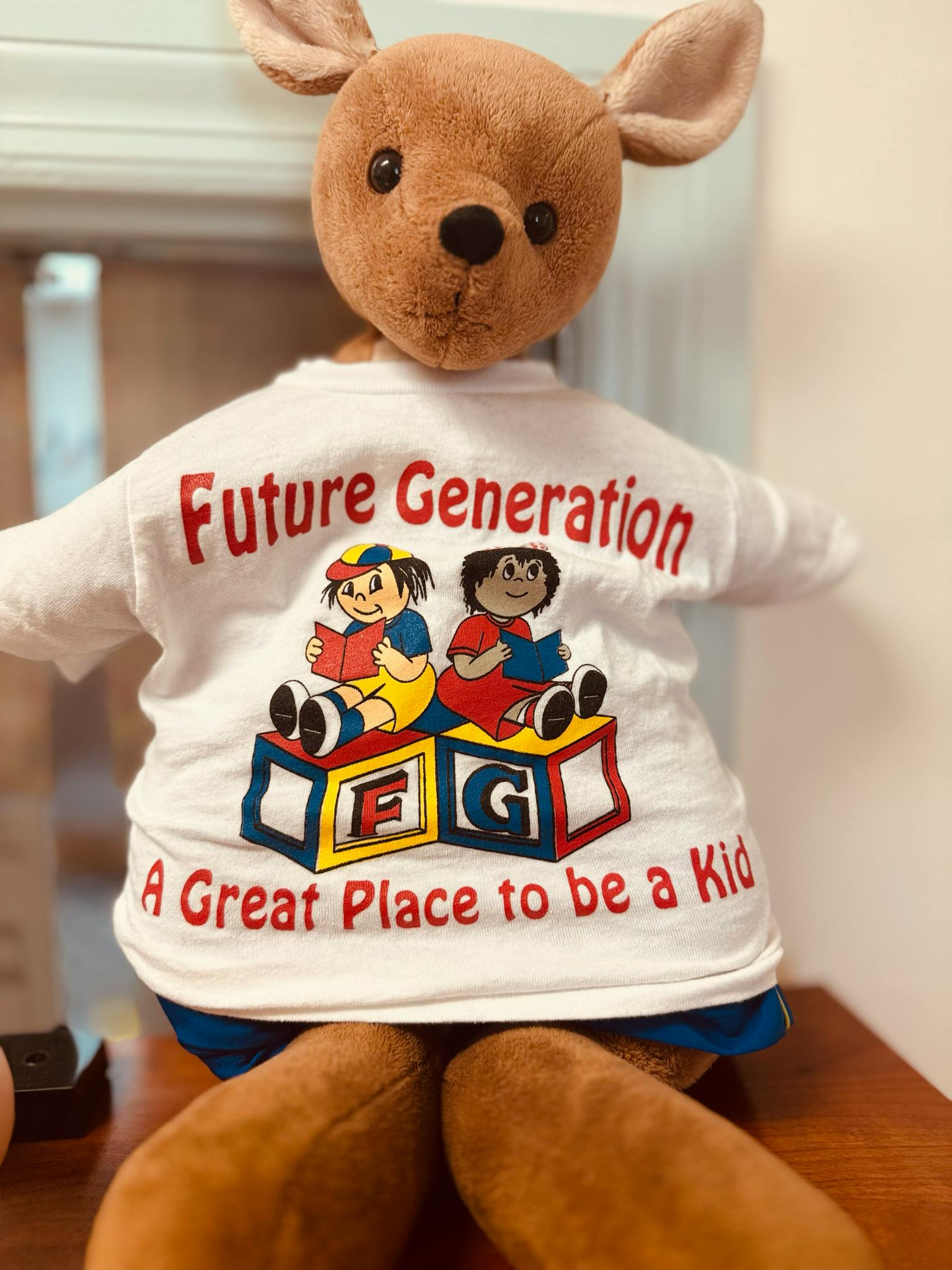 Stuffed animal wearing a white shirt with "Future Generation A Great Place to be a Kid"
