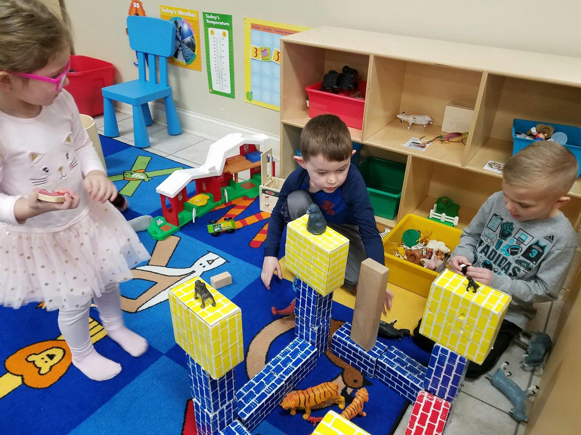 Three children playing with blocks and toys on a blue rug