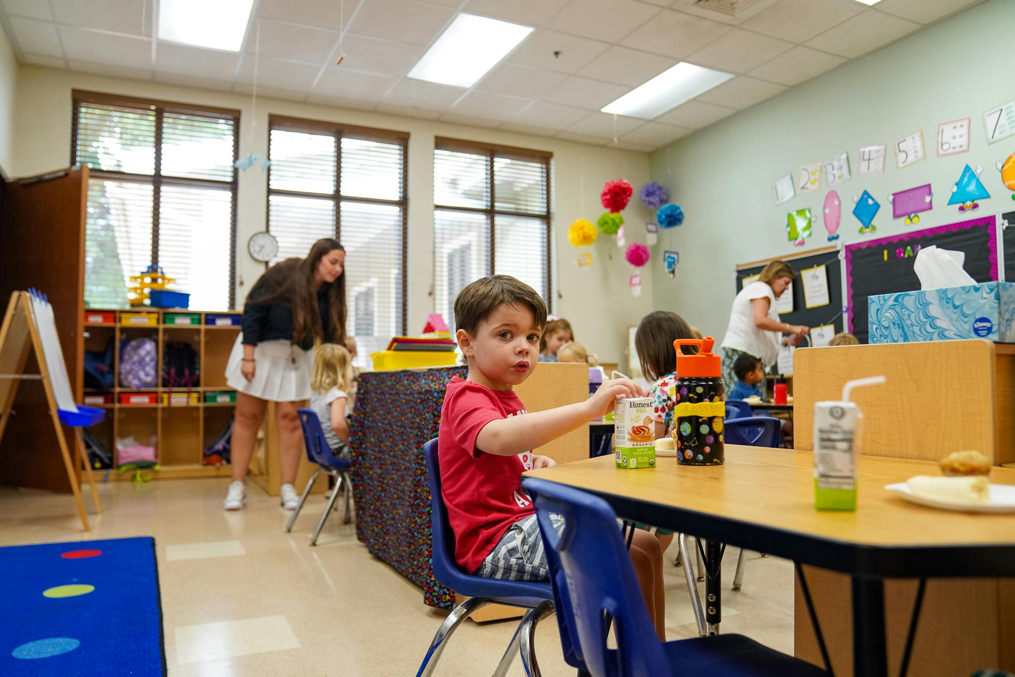 Child in red shirt sitting at a table in a classroom