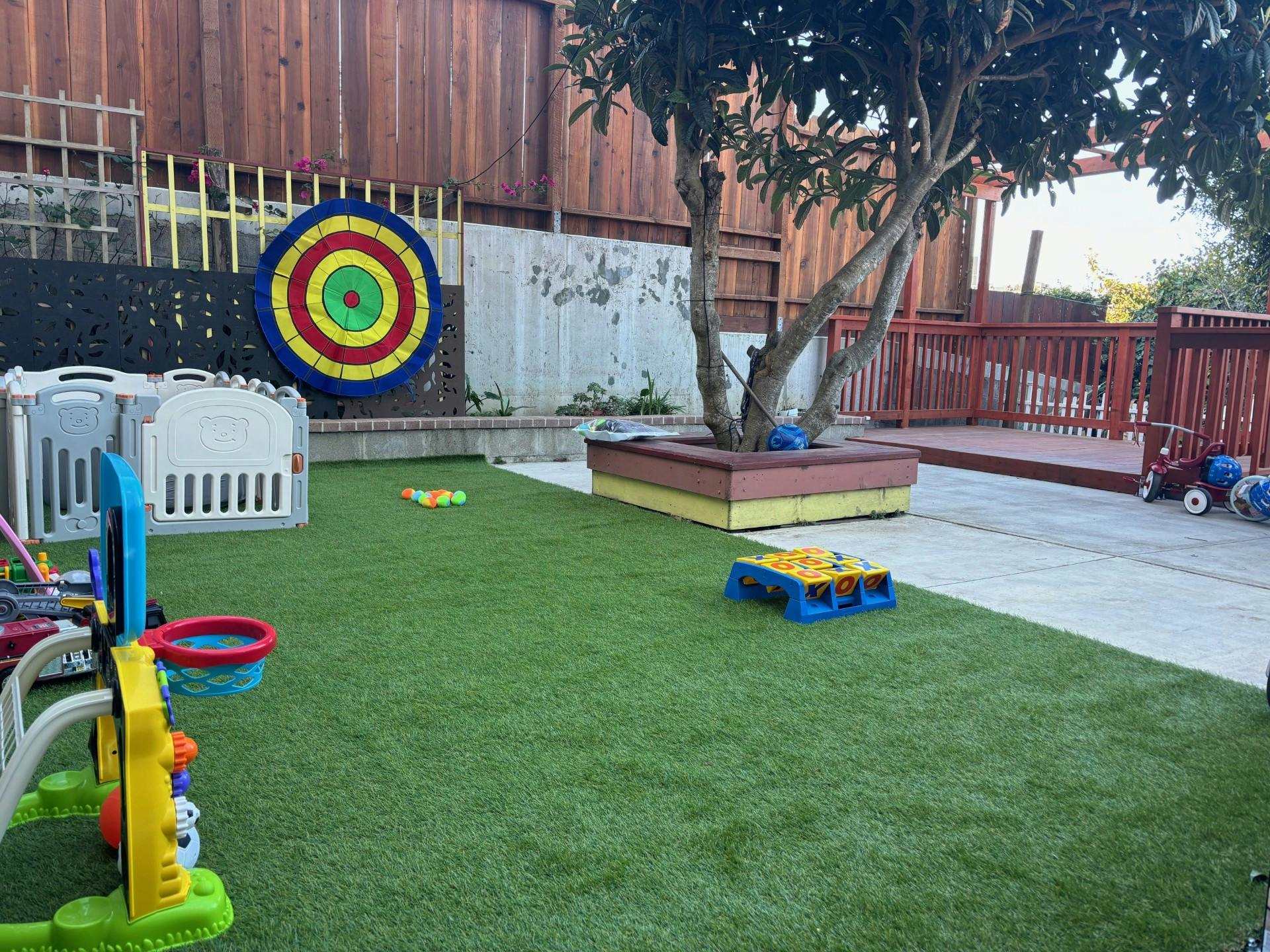 Outdoor play area with artificial grass, toys, and a tree