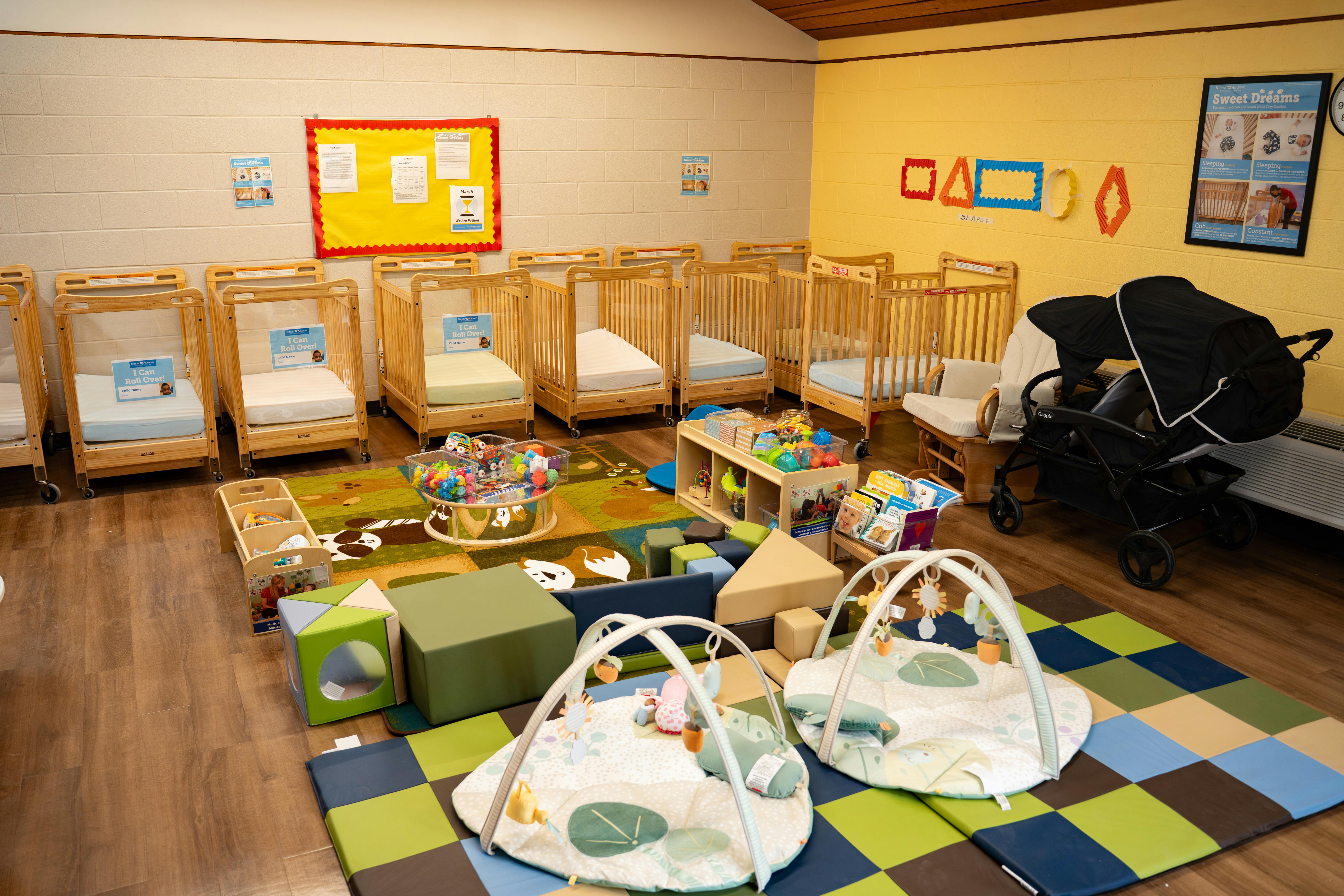 A brightly lit nursery room with multiple cribs, play mats, and toys