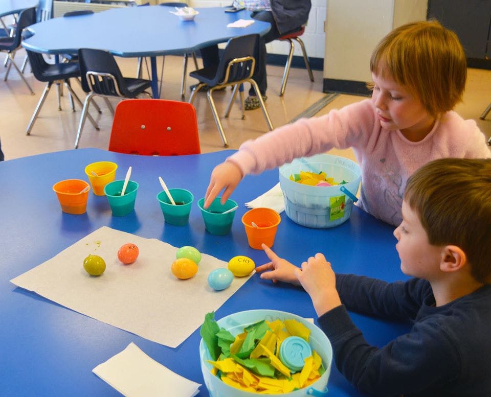 Two children at a table with colorful cups and painted objects
