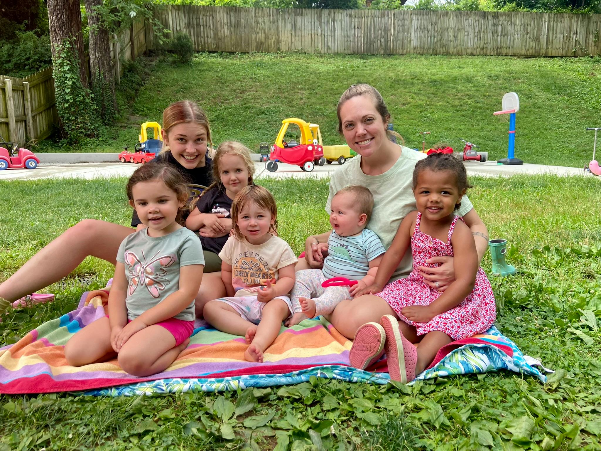 Adult and multiple children sitting on a blanket outdoors