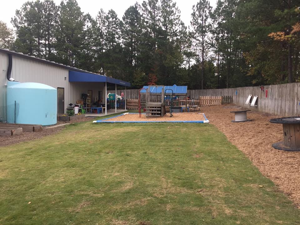 Outdoor playground with a building, blue water tank, and wooden fence