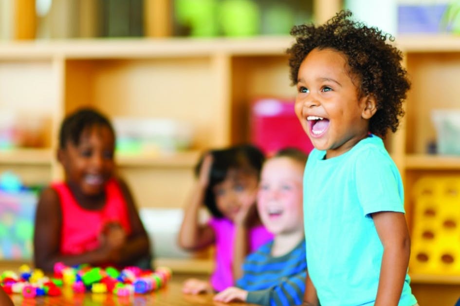 Child in a blue shirt laughing with other children in a classroom