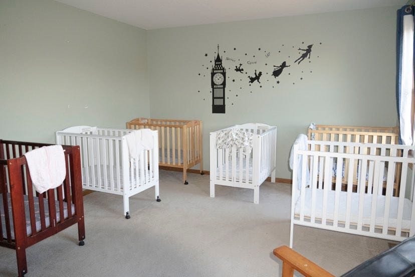 Multiple cribs in a room with a wall decal of a clock tower and flying figures