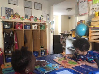 Two children looking at books at a table in a classroom