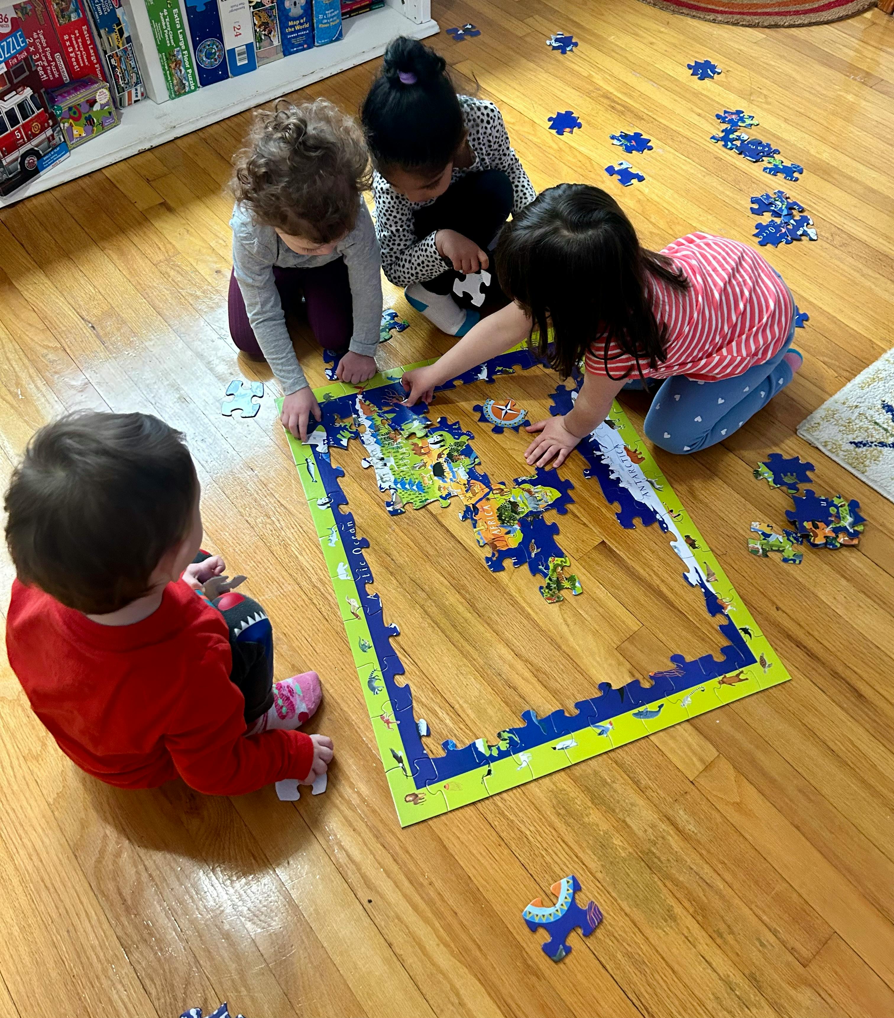 Four children on a wooden floor assembling a large floor puzzle