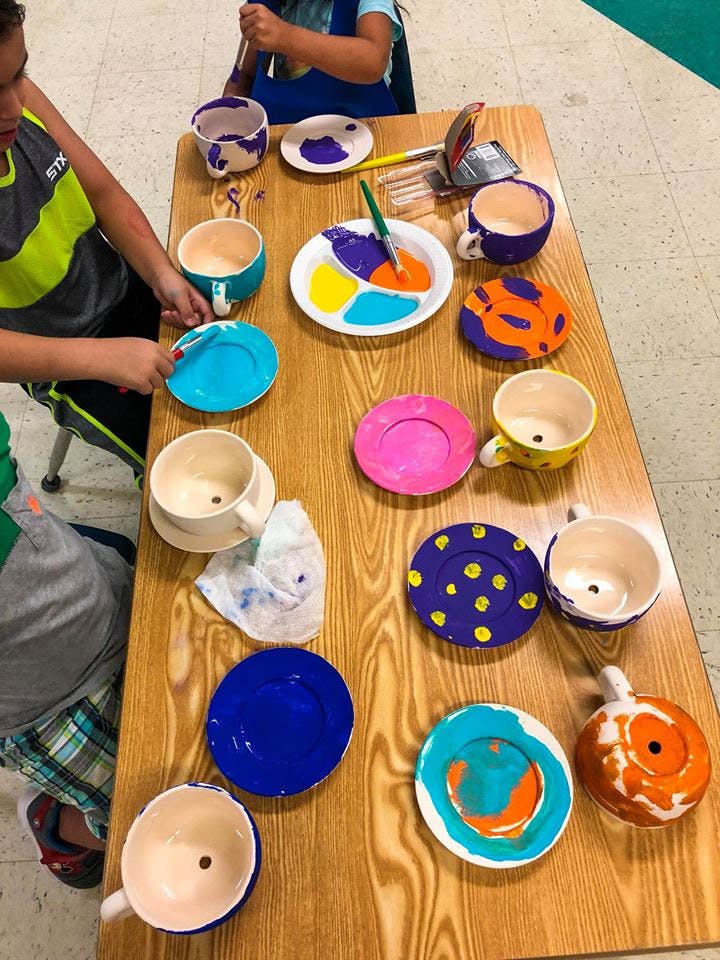 People painting ceramic cups and plates on a wooden table