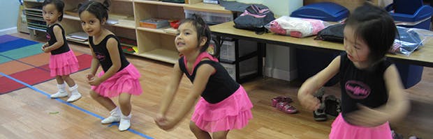 Four children in black tops and pink skirts dancing