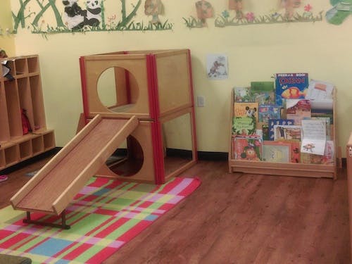 Indoor play structure with a slide and a bookshelf in a classroom