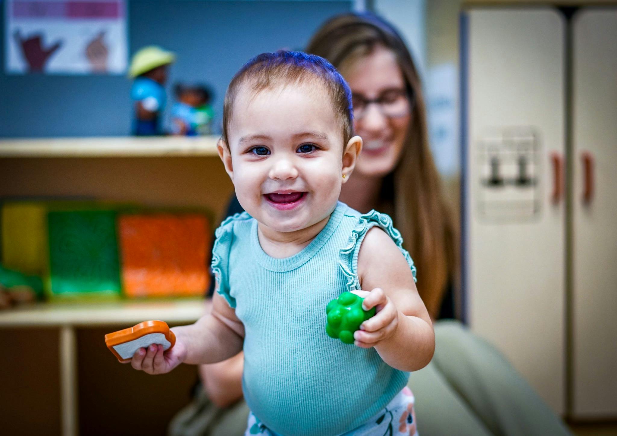 Child holding toys with a person in the background