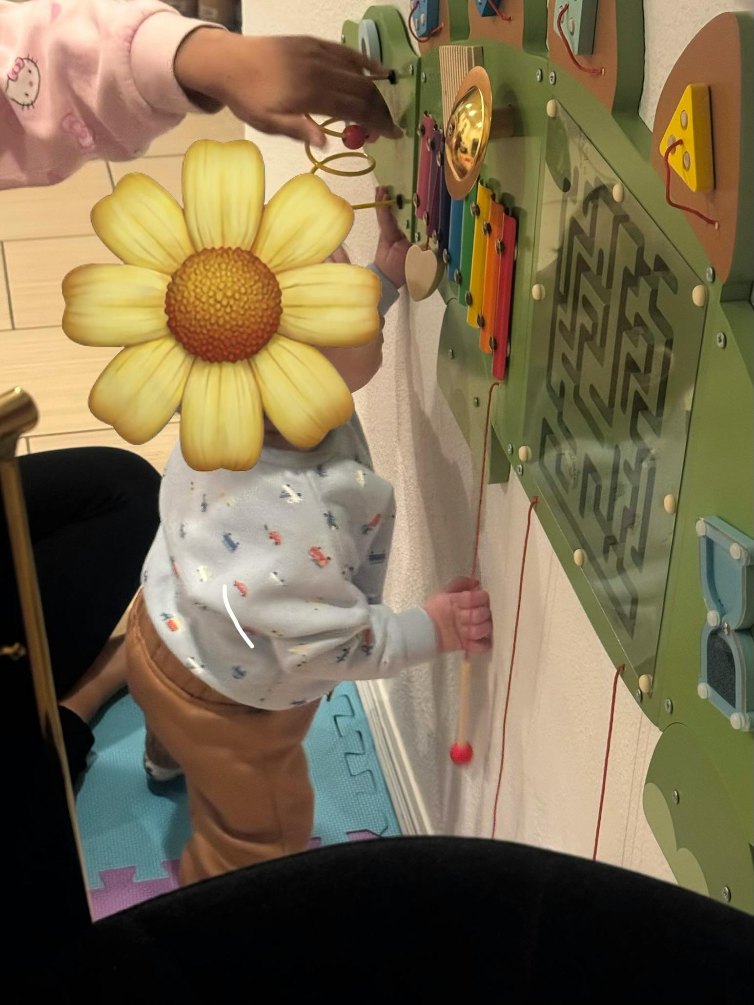 Child standing on a play mat interacting with an activity board with multiple hands
