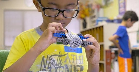 Child in glasses building with toy blocks in a classroom