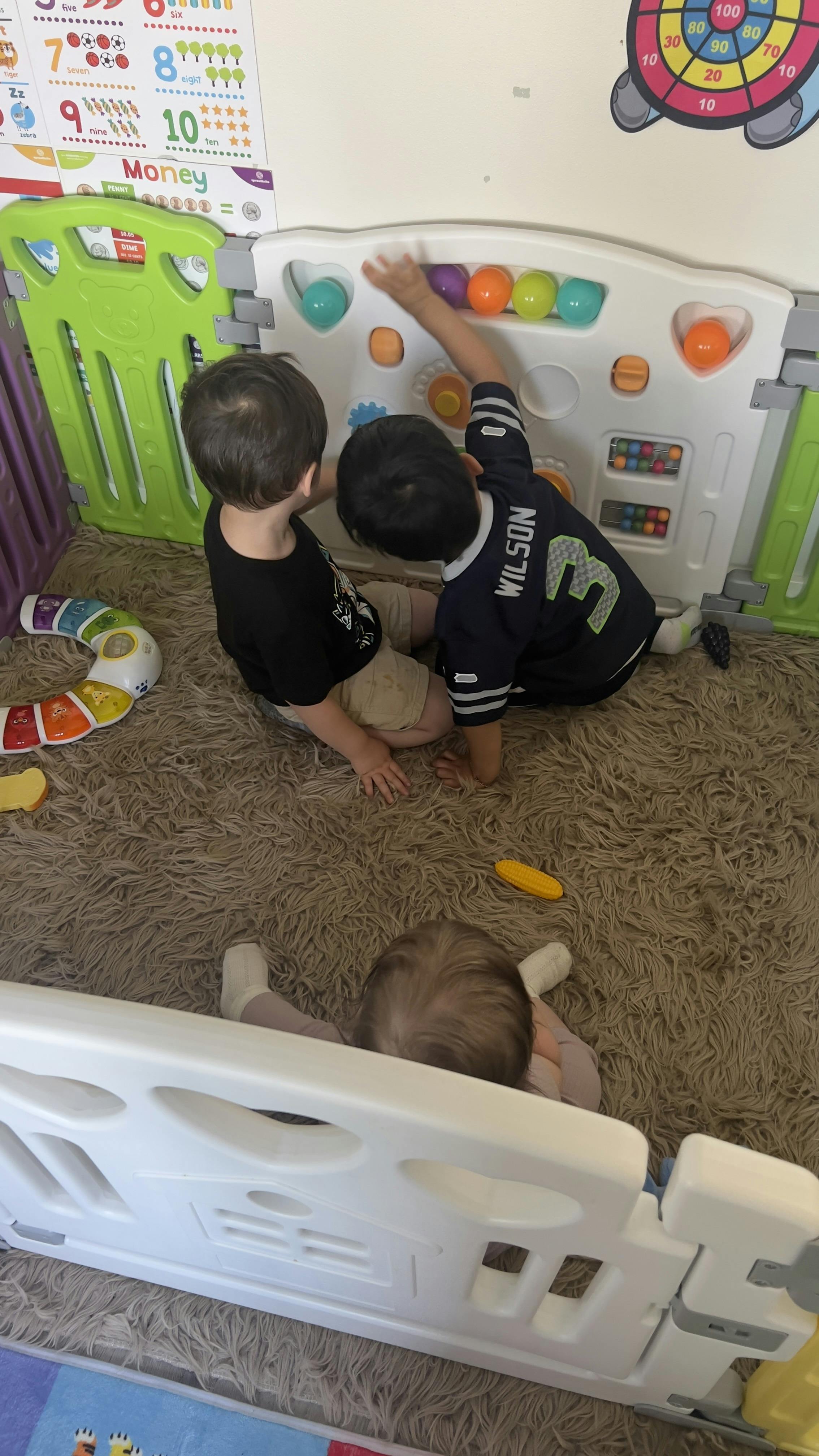 Three children playing in an indoor playpen with colorful balls