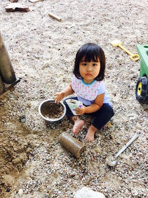 Child playing in sand with a bowl and small container