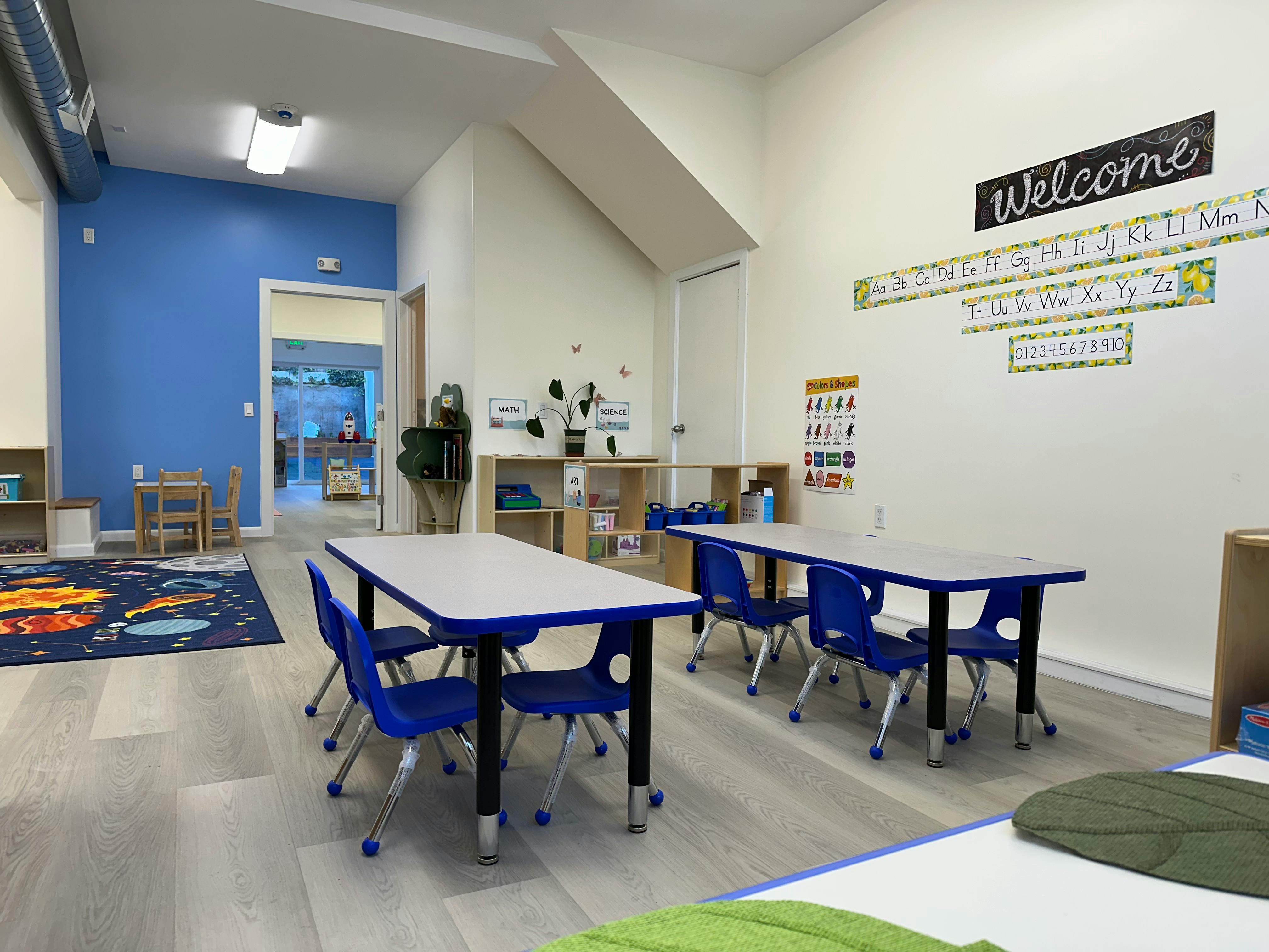 Classroom with small tables and chairs, a welcome sign on the wall