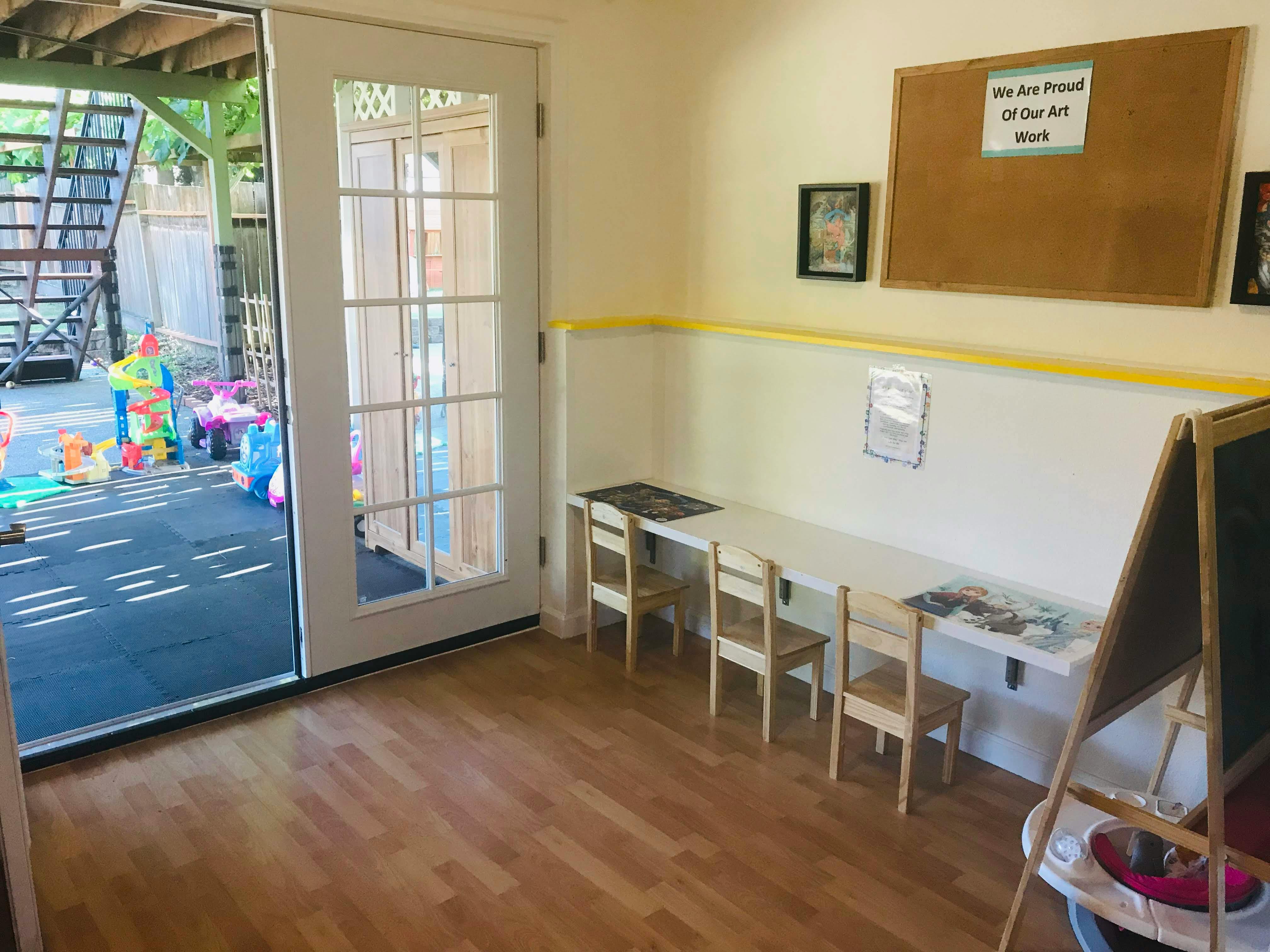 Classroom with small tables and chairs, open door to outdoor play area
