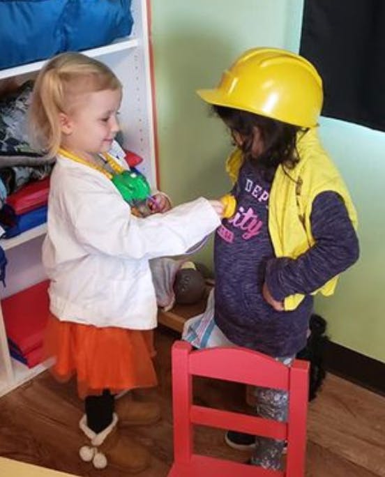 Child in doctor costume examining another child in a hard hat