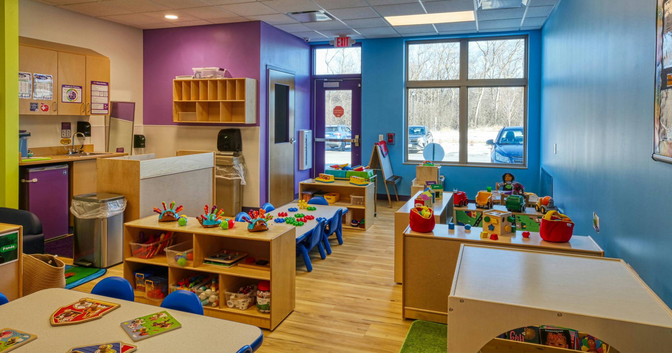 Colorful preschool classroom with tables, chairs, and shelves full of toys