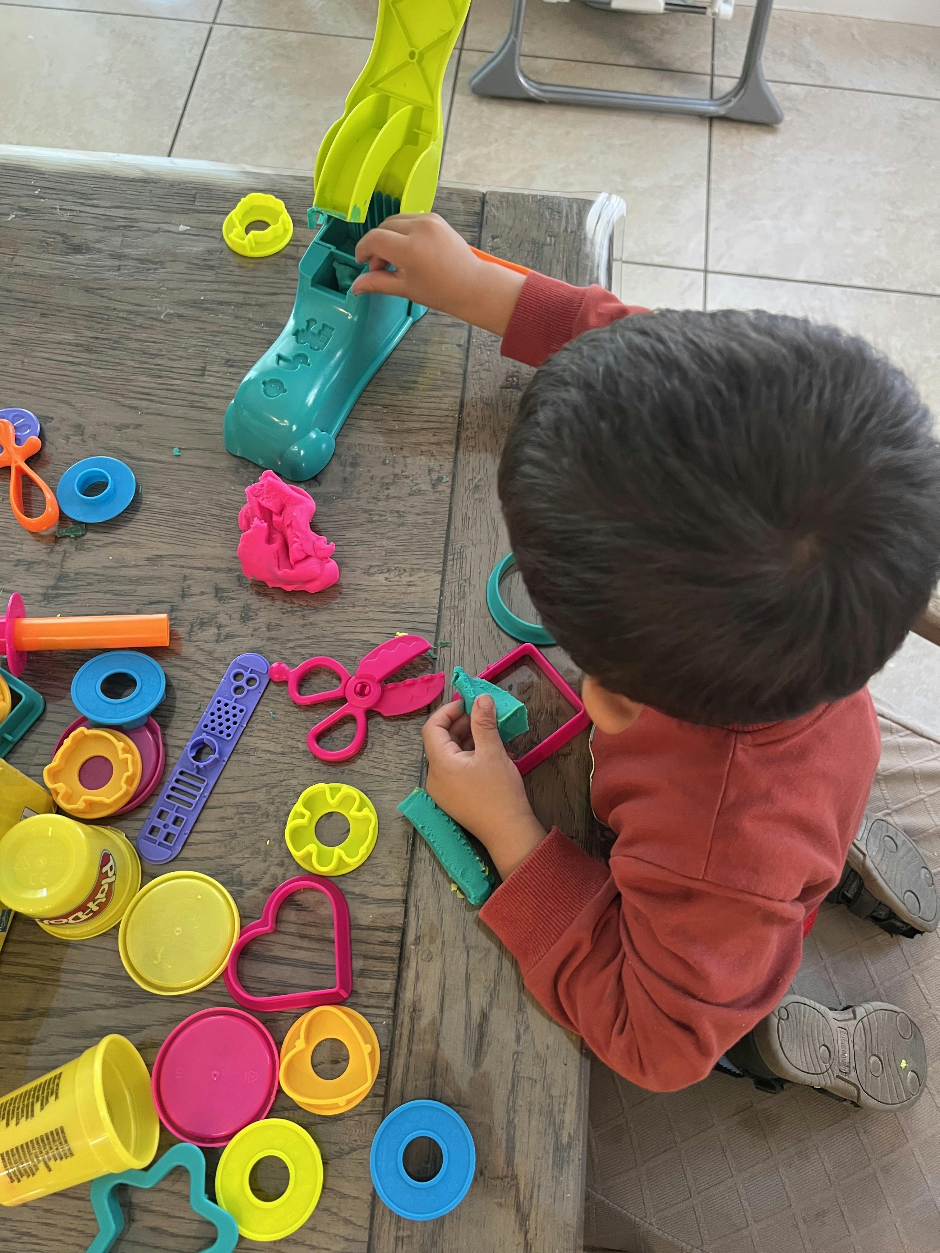 Child playing with modeling clay and plastic tools on a table