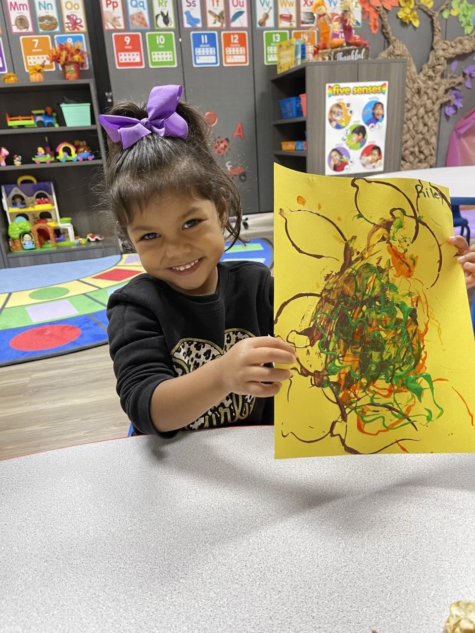 Child holding up a yellow paper with abstract art in a classroom