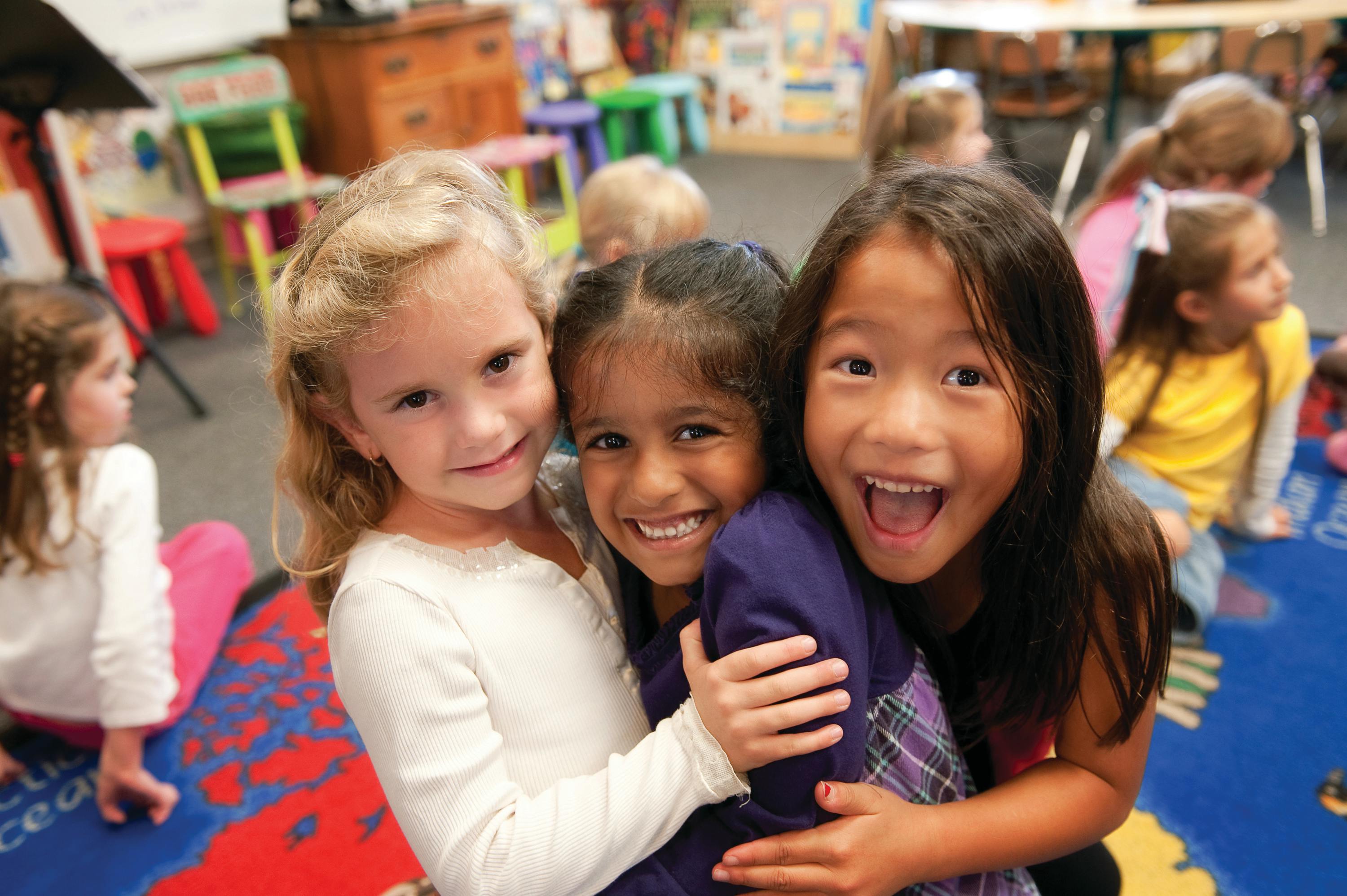 Three children hugging in a classroom