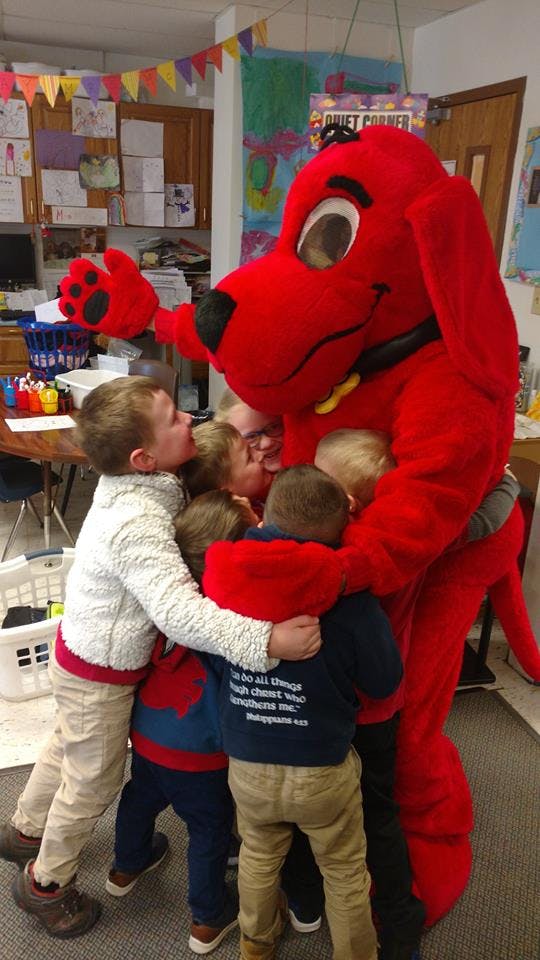 Children hugging a person in a red dog mascot costume in a classroom