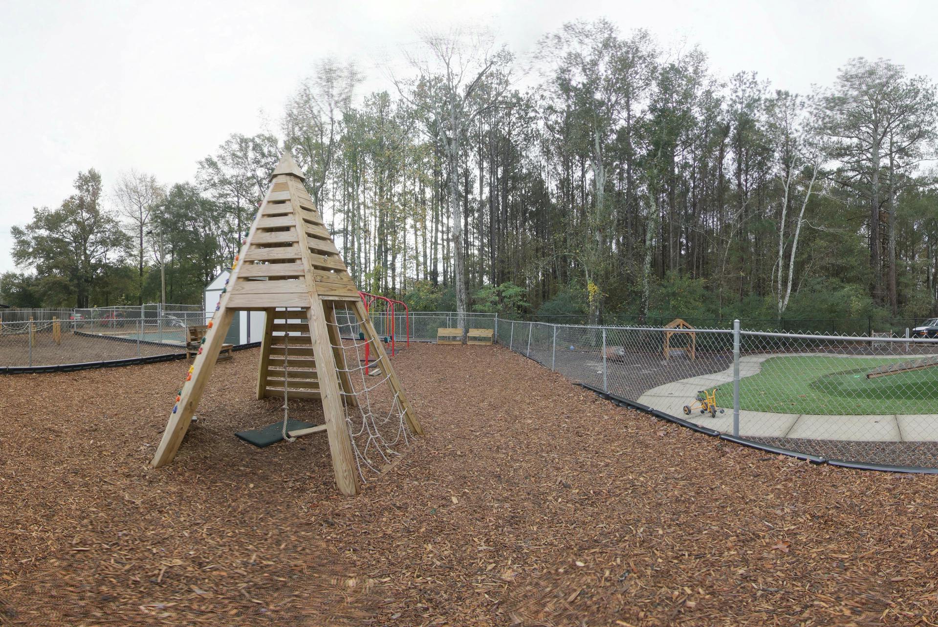 Wooden playground structure with climbing ropes and a swing on wood chips