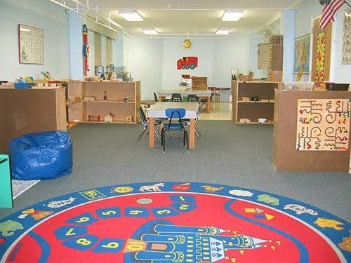 Classroom with small tables and chairs, shelves, and a colorful rug