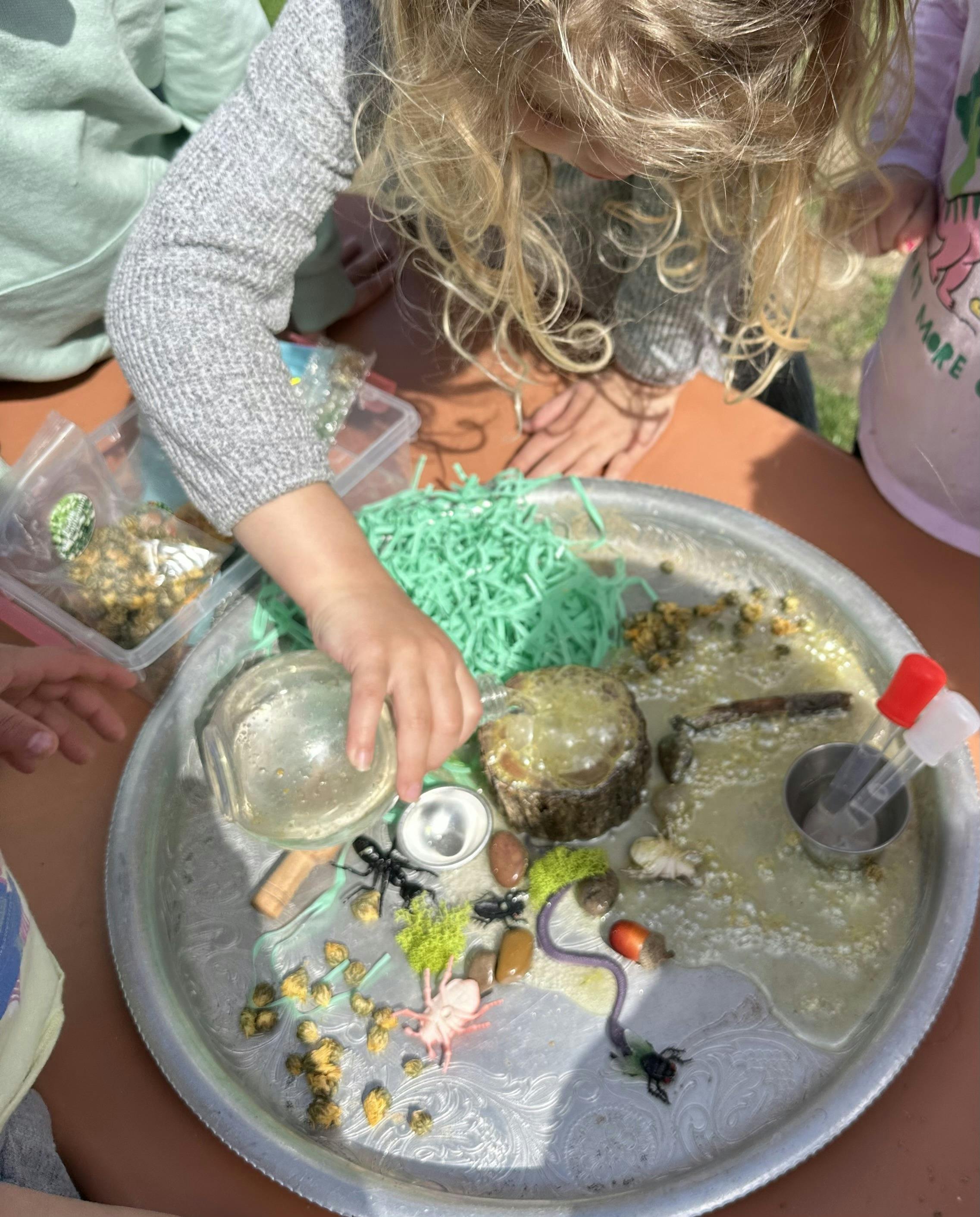 Child's hands playing with items on a silver tray with water