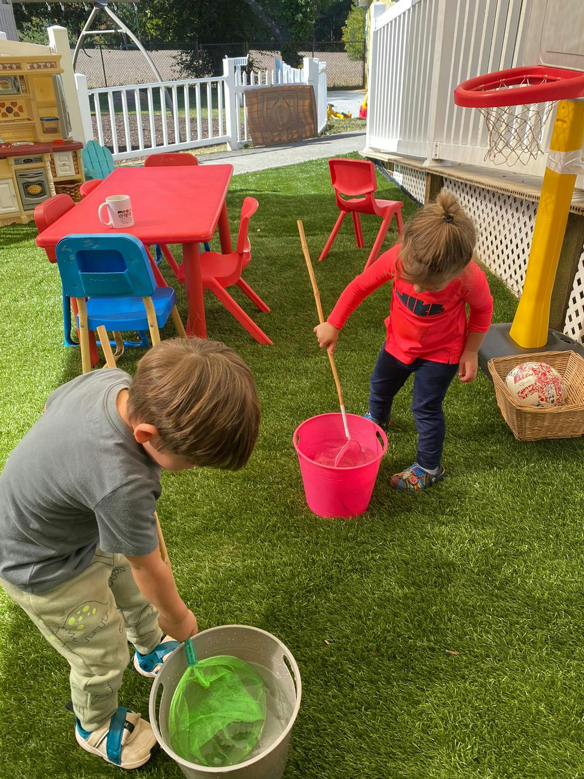 Two children playing with buckets and sticks on artificial grass