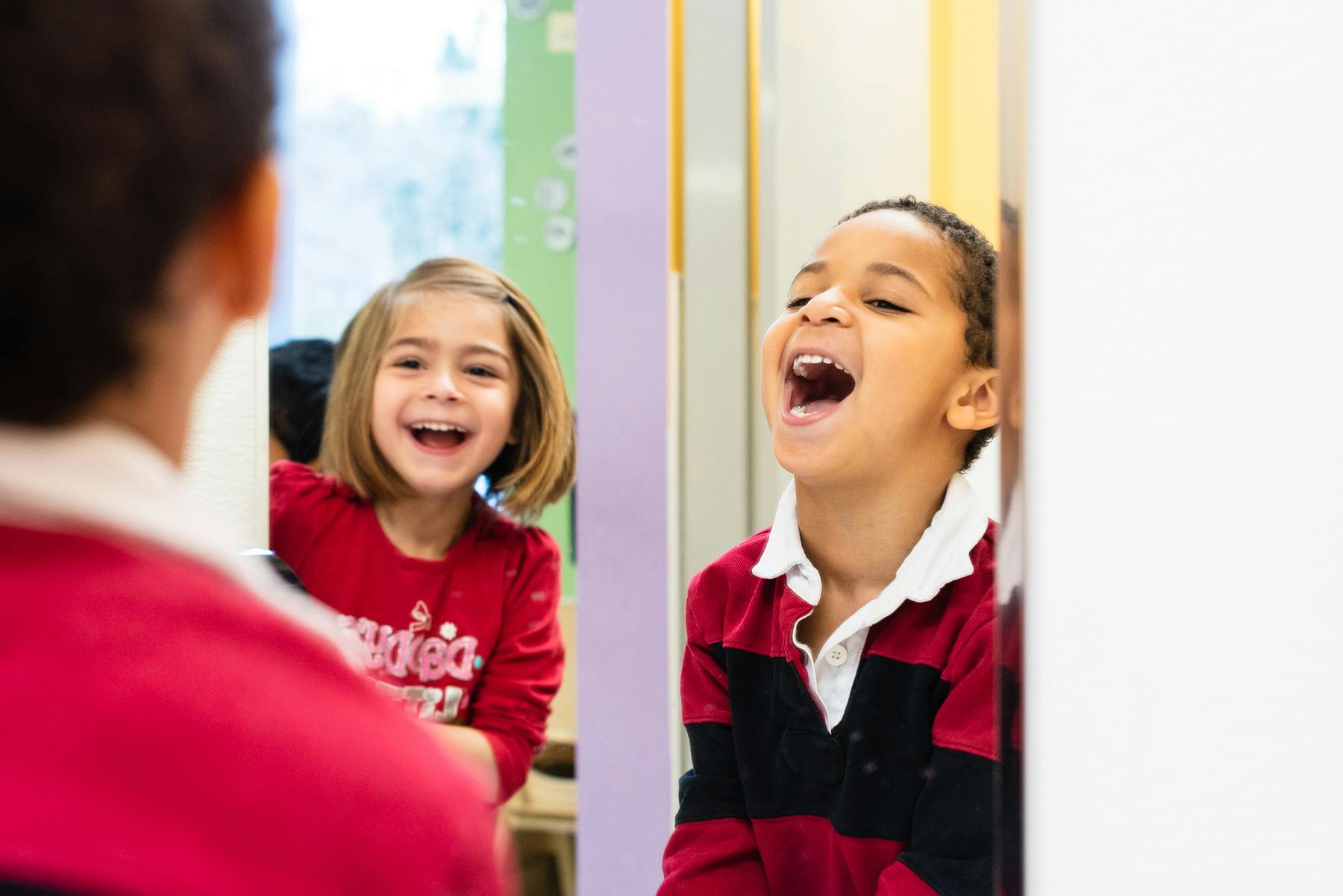 Two children laughing, one seen in a mirror reflection