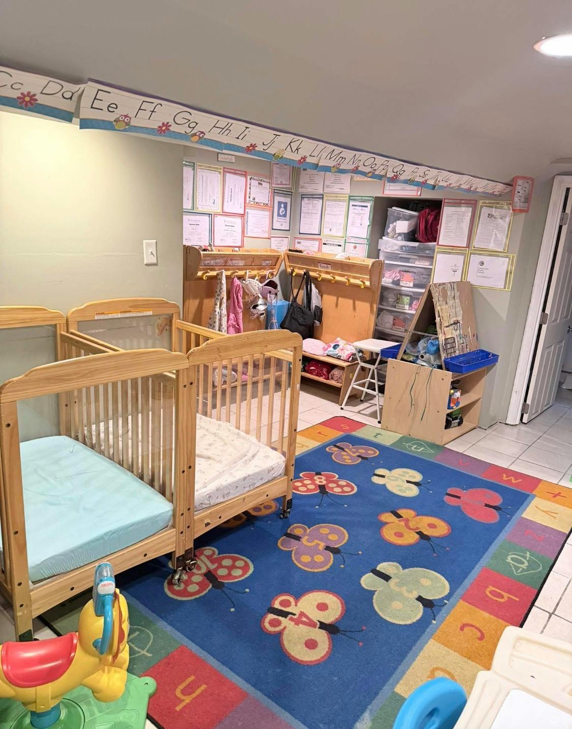 Two baby cribs and a butterfly-patterned rug in a childcare room