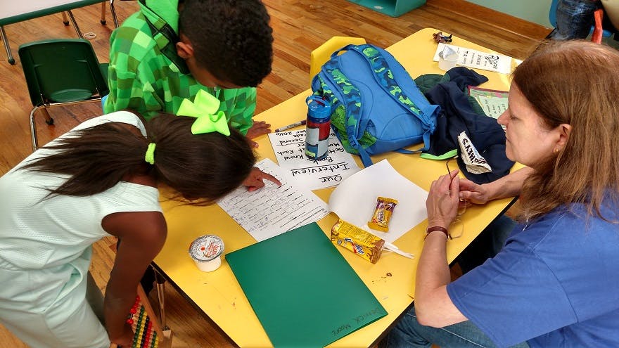Adult and two children looking at papers on a table in a classroom