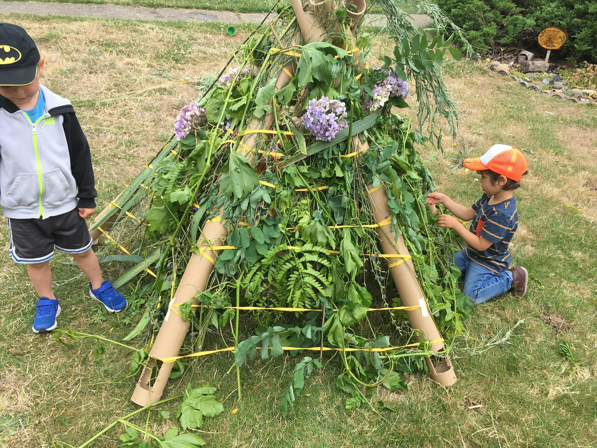 Two children building a teepee-like structure with branches and leaves