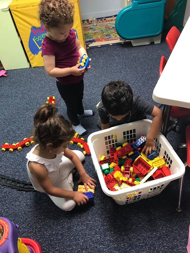 Three children playing with building blocks on a carpeted floor