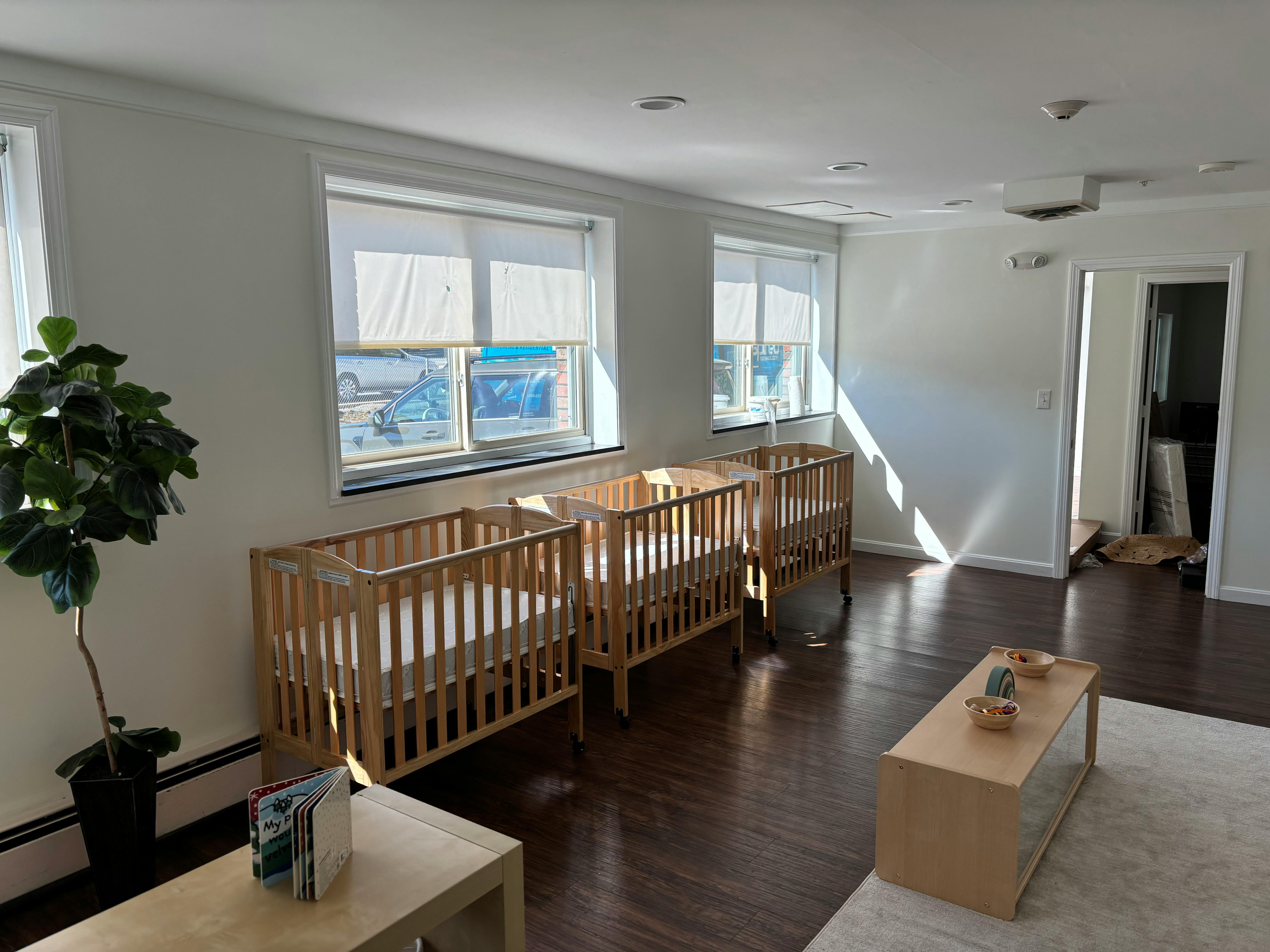 Three wooden cribs in a room with windows