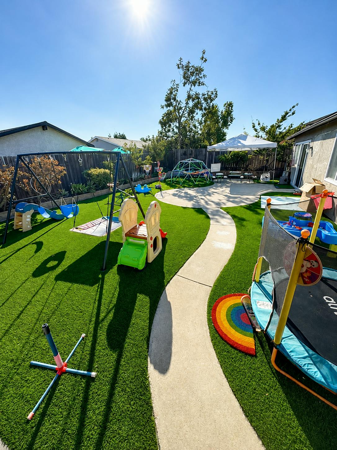 Backyard playground with a swing set, climbing dome, and small trampoline