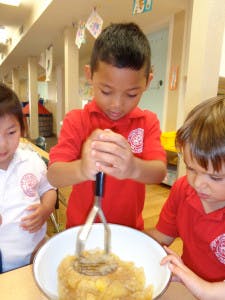 Child mashing food in a bowl with other children nearby