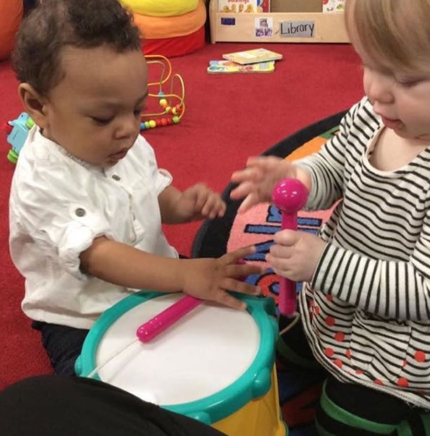 Two children playing with musical toys, one with a drum and the other with a maraca
