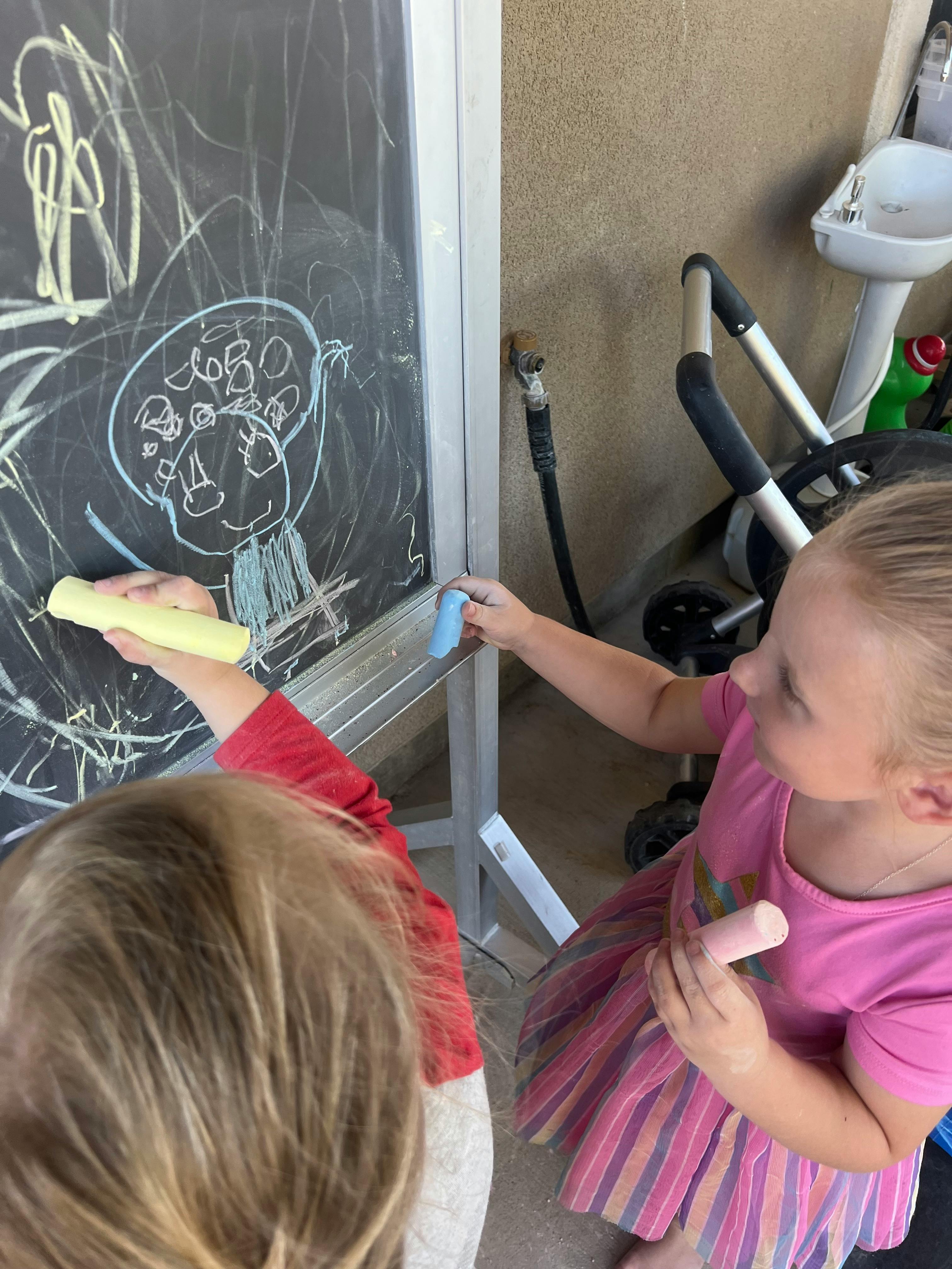 Two children drawing on a chalkboard with chalk